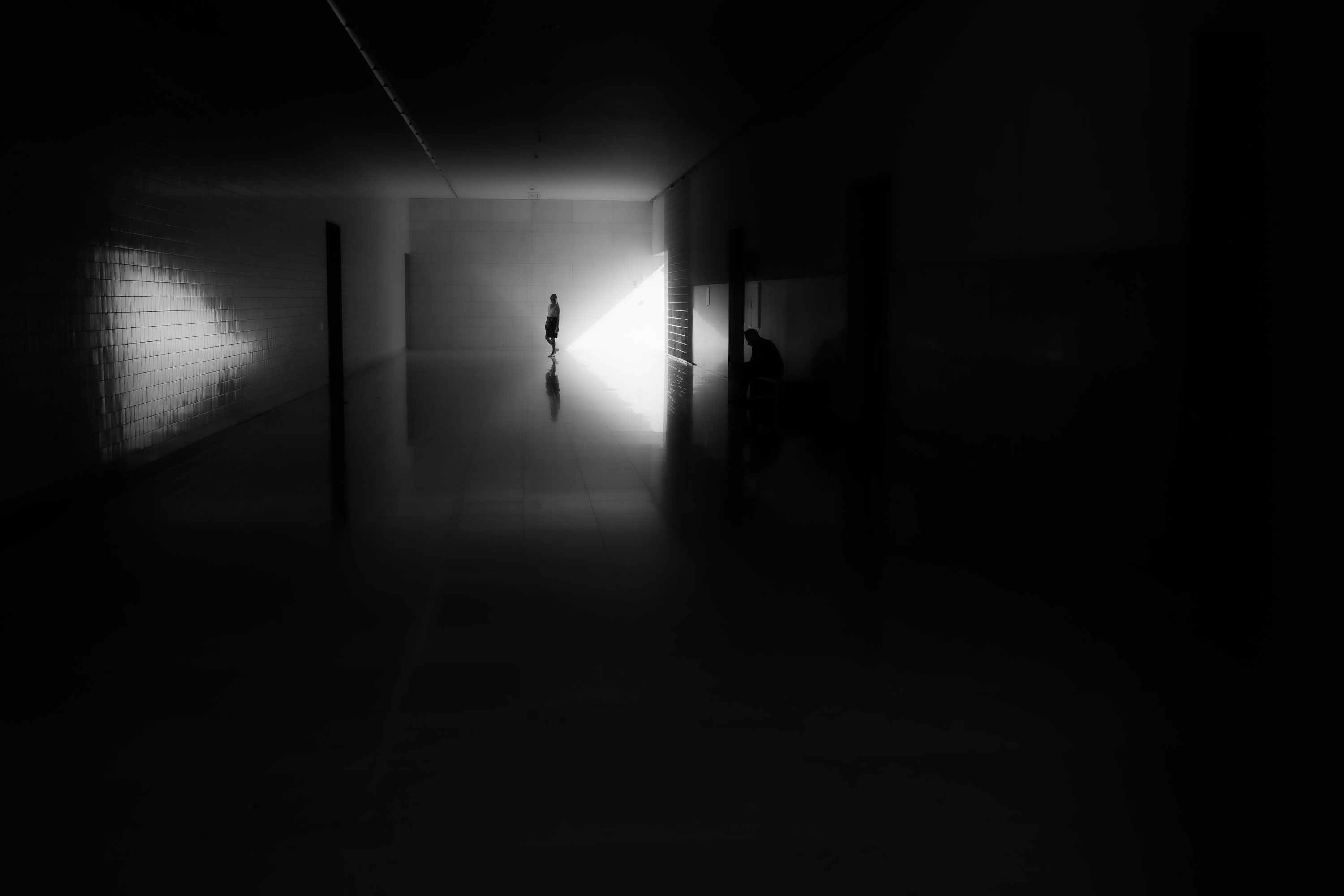 Une silhouette solitaire se tient dans un couloir brillamment éclairé.