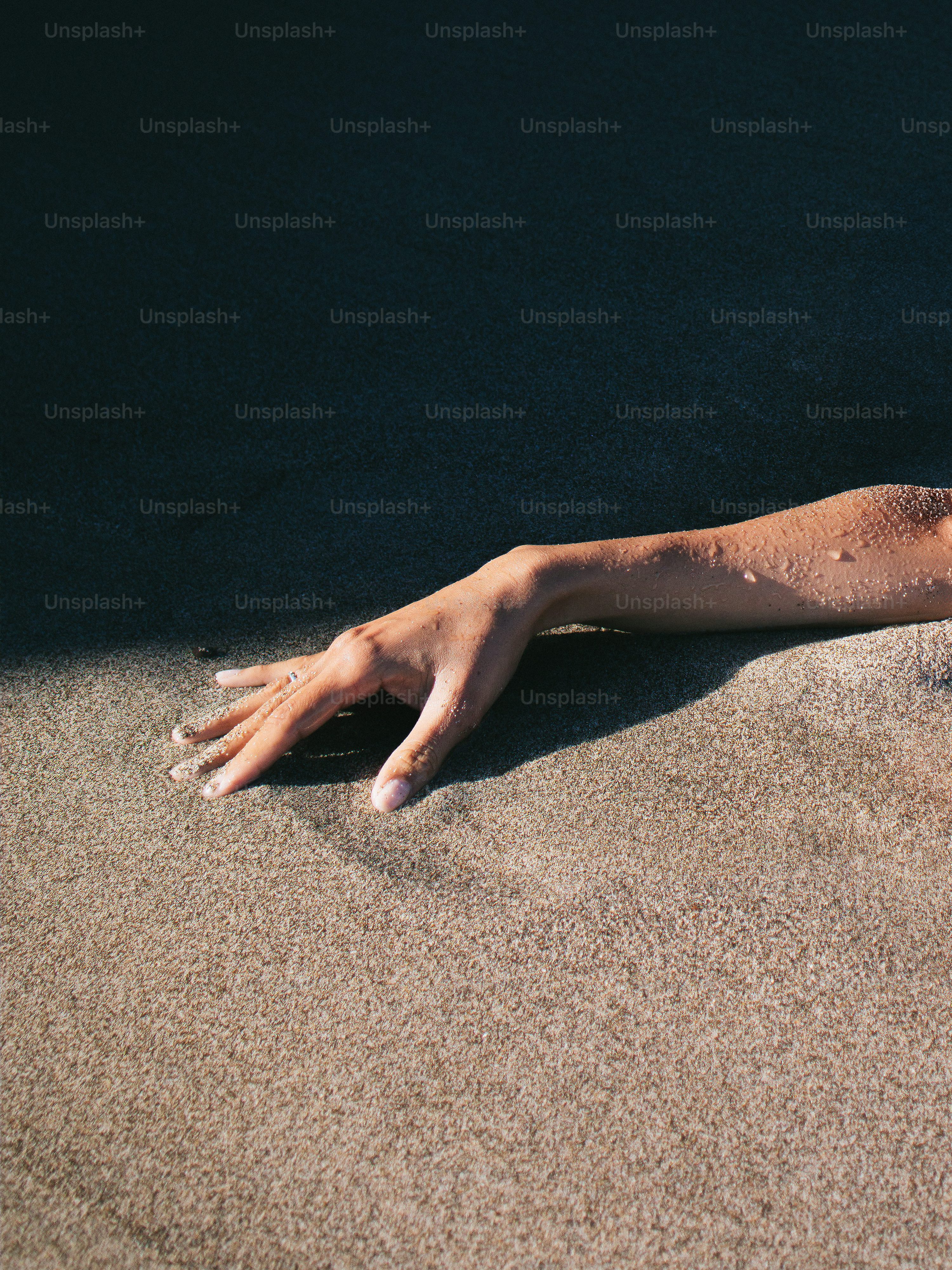 Main émergeant du sable sombre sous la lumière du soleil